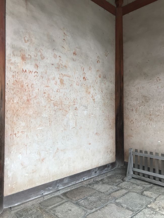 唐招提寺の入り口の壁。酷いな。<br /><br />朱色の塗料が手に付くので、それで手形をつけたり落書きしたりしてあるのです。マジックペンで夫婦二人とその子の名前を書いたものもあります。子の名前の横に（天国）とあるので、お子さんが亡くなったのでしょうが、このようなことをして良いわけがありません。<br />だいたい、『天国』はキリスト教の概念ですから(~_~;)<br /><br />たまに、仏像や重要な建造物などに落書きがあったとニュースになると、それを発端に、あそこのお寺でもあったとか、こっちの神社にもあるとか盛り上がりますが、騒ぐだけ騒ぐといつしかその話題は聞かなくなります。<br />でもそれは、事態が収束したり、落書きをする人がいなくなったりしたわけではなく、ただ単に飽きてマスコミが取り上げなくなっただけ。<br />今もこうやって落書きは存在しているのです。<br />