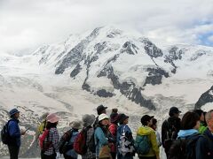 ゴルナーグラート展望台に到着しました。なのに展望台の全景写真が無い。
う、う、う。山の景色ばかりに目が行ってそこまで気が付きませんでした。
でも展望台は人だらけだったな。写しても多分人しか写らなかったと思います。でもどの位の広さなのかは分かったかも。
せめて展望台の敷地と観光客の足だけでも写しておけば良かったな。
さて、展望台に全員が集合するとトレッキングガイドから周囲の山に付いて説明がありました。
貰ったゴルナーグラート展望台の小パンフには北と東の山のイラストがありません。
またパノラマ写真はあるけれど山の名前が無い。かりにあっても山の頂上が雲に隠れているためパンフの写真と違うためどの山か分からない。
ガイドさんの指し示す方を見て納得したつもり。やはり快晴の下でこの展望台に立ちたかったな。
一通り説明が終わると20分の写真タイムとなりました。この間にクリムホテルで手洗いを終えてゴルナーグラート駅前に集合しないといけません。急いで行動しないと間に合わないかもしれない。
解散と同時に始まったのが記念写真。一組ずつ展望台の端に立って写してもらいます。36名のツアーなので記念撮影には時間がかかります。順番が早ければ影響はありませんが後ろの方であれば待っている時間がもったいない。
私は記念写真をパスしてこの時間に山の写真を撮りまくりました。
