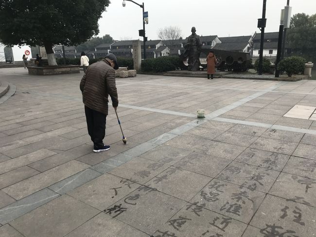 橋を渡り、戻ってくると、広場に水で字を書く人が。