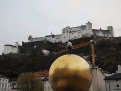 更に進むと、、広場Kapitelplatzがあり、、
「ホーエンザルツブルク城」がきれいに見えます、、

そして、、「Sphaera(スフェーラ）」
現代ドイツを代表する彫刻家シュテファン バルケンホール(1957～ )の芸術作品
”Sphaera(スフェーラ)"とはラテン語で”球”を表し、その”黄金色の球”の上に人が立っています、、

高さ9mの場所に立っている男性ブロンズ像は、何を見ているのでしょうか、、

さあ、、この「Sphaera(スフェーラ)」から真っ直ぐ進むとケーブルカー乗り場は直ぐ、、
