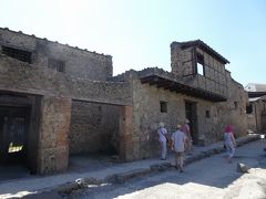 REGIO I
Casa del Menandro
メナンドロの家

※この大きな建物は建築学的に複雑な変遷を経ていて、身分の高い一族の典型的な住居の好例です。アトリウムには「イリアス」と「オデュッセイア」の場面が描かれています。ペリスティリウムはロードス式で、北側の部分が他より高くなっています。 家の名前は、ポルティコに飾られていたアテネの喜劇作家メナンドロの肖像に由来しています。この家には小さなテルメ施設があり、その下にはおそらくは貯蔵室であったかと思われる地下室があって、そこから118もの銀製品が納められた箱が見つかりました。発見された品々は現在ナポリの国立考古学博物館に収蔵されています。 この宝は修復工事の前に隠されたもので、家族の食事のサービスに使用された銀器でした。 これらの食器の中には葡萄酒用のピッチャーも含まれていまし
たが、饗宴用の杯や皿が主なものでした。 南側には仕上げの施されていない空間があって、復元された馬車が展示されています。この家はポッペイ一族のクイント・ポッペオ・サビーノの所有によるもので、ネロ帝の2番目の妃ポッペア・サビー
ナの親戚でした。発掘時期： 1928; 1930; 1932.

２階に出窓が残っている。