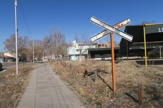 なんて簡素な踏切標識・・・海外だと良くみますね！<br />右手の緑のブツ（駐車場）の間を丸埋されていないレールがぶった切っています。