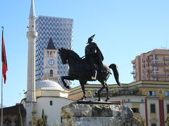 　オスマン帝国に抵抗したアルバニアの英雄、スカンデルベグ。平日の昼間だというのに、スカンデルベグ広場は、沢山の人間で賑わっており、逆にその光景が不気味に思える程だ。辺りを360度見渡して、手持ちの地球の歩き方の地図と整合する。基本構造が頭に入ったところで、今日の宿と、マケドニア行きのバスのチケットを買いに旅行代理店へ向かう。

　マケドニア行きバスのお店は、かなり目立つ看板のお陰ですぐに発見する事が出来た。人の良さそうな英語の出来る女性が、テキパキとチケットをアレンジしてくれた。