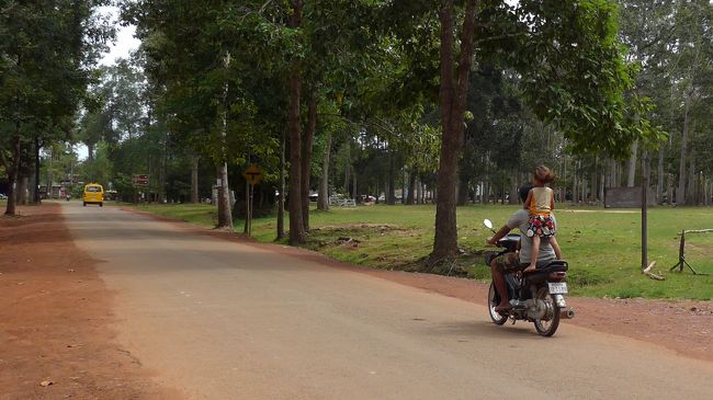 ７＜ナイス立ち乗り＞<br />小さい女の子が、見事な姿勢でバイクの立ち乗り。<br />カンボジアでは子どもがバイクを運転しているのを何度か見た。何と、運転免許制度はないんだって。本当？