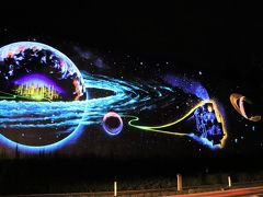 この壁画は“未来都市銀河 地球鉄道壁画”と呼ばれて、高さ10m、長さ80mの道路脇の壁に夜間しか見ることの出来ない特殊な塗料で描かれています。  