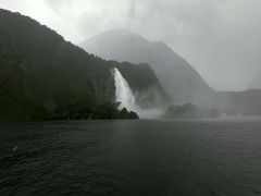 奥に見えるのがボーエン滝です。こちらもすごい水量。

右奥に船着き場が見えてきました。２時間弱のクルーズ、雨で風もすごくて天候には恵まれなかったけど、雨天ならではの迫力ある景色が見られて、本当に自然のパワーの素晴らしさを感じられました。雨で良かったのかも。

でもやっぱり、晴れも見たい、、、！


そして、帰りは思い切ってセスナでクイーンズタウンまで戻るオプションを追加していました。往復８時間のバス移動はちょっとしんどいから…
空から見るミルフォードサウンドやワカティプ湖の景色を楽しみにしていたのですが、、、

この悪天候により、セスナの飛行はできないとのことでバスで帰ってねと言われました。残念すぎる。
まあでもこの天候なら仕方ないですよね。揺れたりするの怖いし。

おとなしくバスで帰りましょう。