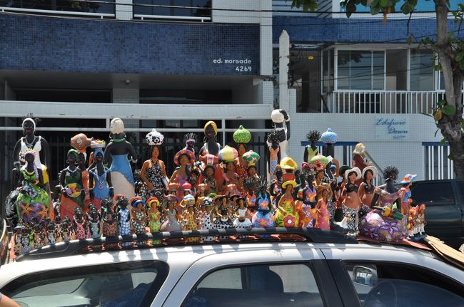 このエリアはサルバドールの一番身近なリゾート地で海水浴客でにぎわっている。海岸沿いにはおしゃれなレストランやペンションなども多い。<br /><br />路上では停められた車の上にバイーア人形を並べて売られていた。