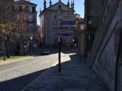 さてさて、お昼を満腹食べたあとはさらにドン・ルイス一世橋をめざします。天気も快晴、風はひんやりとさわやか、昼ワインでいい感じです。こんな毎日を過ごしていると本当に癒されます。仕事と人間関係、納期と品質に忙殺される日本から遠く離れたポルトの地で人としての生き方を思いだしたりしています。
ここはボルサ宮殿の横の道です。右手がボルサ宮殿、正面がParish Church of St. Nicholas、見えてませんが左手がインファンテ・ドン・エンヒーケ庭園。
標識の一番上にドン・ルイス一世橋の方向が示されています。でも、２０年１２月現在でおんなじ看板をストリートビューで見ると白塗りになってますがなぜ？
で、ドン・ルイス一世橋に向かう前にボルサ宮殿に隣接しているigreja da ordem de s.francisco（モヌメント・デ・サン・フランシスコ教会）に寄ります。