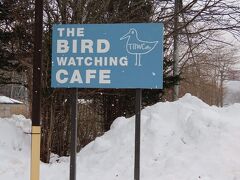 青い看板が目印です。10時ちょうどに到着しました。
カフェスペースと撮影スペースと分かれていて、今日は私たちは撮影スペースを予約しています。
カフェの方は屋内ですが、撮影スペースの方は、窓ガラスが入っていない部屋になっていて、撮影用の座席が並んでいます。予約はネットでできますが、8席の中でも席指定したい時は電話で希望の番号を伝える二重予約システムを取られています。
店内には写真家の方のギャラリーが併設されていて、アカショウビンやヤマセミの迫力の写真が展示されています。