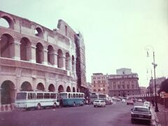 1974年のローマ　古代ローマ帝政期、西暦80年に建設された巨大円形闘技場、ローマを象徴するコロッセオ。最上階には、ポールが立てられていた穴が残っています。上部を覆う日差し除けの天幕を張るためのものでした。現代の開閉式ドームも負けそうですね！　停まっている観光バスもレトロです！！