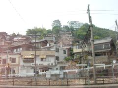 このときは尾道駅周辺の写真は撮影していませんでした。そこで2005年に撮った駅から北側（山側）の写真を掲載します。
海岸沿いから山が切り立ち、斜面に住宅街が開けているのがわかります。
山の上には「尾道城」と「ビュウホテルせいざん」が見えます。この場所にはお城があったことはなく、中は博物館風の観光の建物たったそうです。この尾道城、フォートラベラーのろくおさんの旅行記で拝見したら、今は取り壊されているそうです。随分景色も変化していました。ろくおさんの旅行記はこちら↓
https://4travel.jp/travelogue/11687268
偽物とはいえ、長らく尾道の景色の一部でした。街は時代と共に変化していくものですが、ちょっと寂しいです。