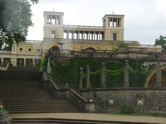サンスーシ宮殿から新宮殿に向かうマウルベールアレーの右側に
オランジェリー宮殿（Orangerieschloss）が見えます。
オランジェリー宮殿は1851年から1864年にかけて、
プロイセン国王フリードリヒ・ヴィルヘルム4世の命により
建てられました。
　2つの塔をもつ中央館は、ローマにある別荘ヴィラ・メディチを
モデルにして造られました。
フリードリヒ・ヴィルヘルム4世は、
ラファエロの絵画を飾りたかったのですが、
オリジナルは入手できなかったので、複製を飾ることにしました。
それが「ラファエロの間」で、複製が50点以上も飾られています。
徳島県鳴門市にある大塚美術館のようなものですね。
　実はこの車道はオランジェリー宮殿の長い庭のど真ん中を
突っ切って通っています。
左側の庭は、車道のすぐ脇に丸い噴水があり、
その先はエプロンのように長く芝生が続きます。
これは、宮殿の屋上から眺めるとちょうどいい長さなのです。