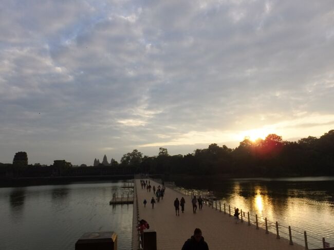 アンコールワットから少し離れた方が朝日も入れたショットの撮影ができる。<br />写真の撮り方もガイドのKOMUROさんにいろいろ習いました。<br /><br />浮橋の手前から環濠を撮影<br />向こうに小さくアンコールワットが見える。