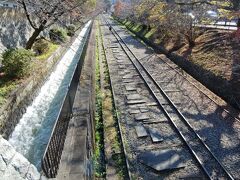 少し戻ると、琵琶湖の湖水を京都へ運ぶ水路「琵琶湖疎水」（左側）とレールが敷かれた「蹴上（けあげ）インクライン」があります。

「琵琶湖疎水」は、明治維新後の東京遷都に伴いよって人口が減少し、産業が衰退した京都に活力を呼び戻すために行ったインフラ整備で、明治23（1889）年に第1疎水完成し、その後、明治45（1912）年に第2疎水が増設されました。
琵琶湖の水を使って発電、上水道整備、船での物資の行き来が盛んになり、特に水力発電による電力供給量の増加で新しい工場が建設され、路面電車が走り、京都は活気を取り戻したのだそうです。

「蹴上インクライン」は、「琵琶湖疎水」が京都と大津間の船の輸送を用途の一つとするなかで、疎水の落差が大きくて船が運行できない蹴上地区に設置された傾斜鉄道です。
台車に船を載せてケーブルカーのようにレールの上を上下させるインクライン方式で全長640m、敷地幅22mあり、上流の「蹴上船溜（ふなだまり）」と下流の「南禅寺船溜」間で明治24（1891）年から昭和23（1948）年まで運用されていました。