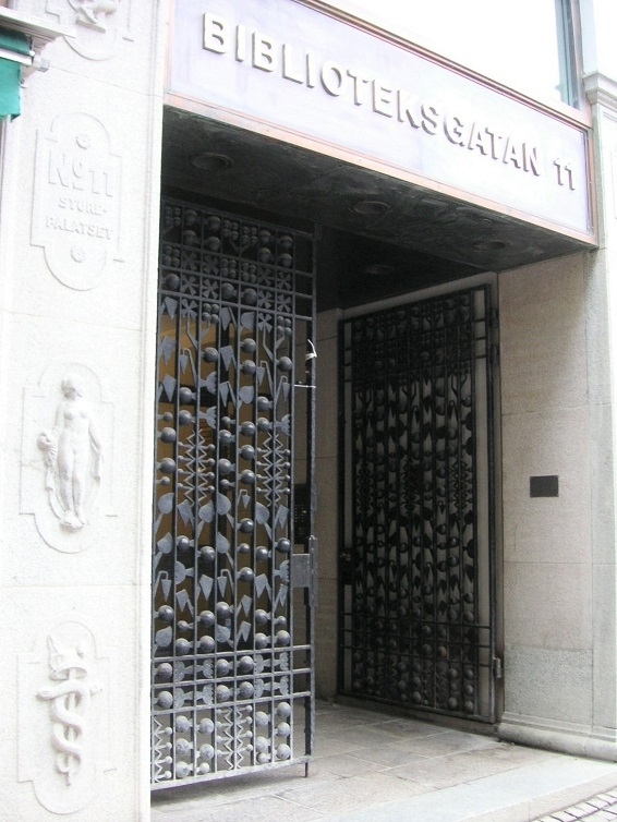 お隣りの鉄細工の扉はアールデコ風でカッコいい！<br />周りの彫刻には、ここにも杖に絡まる２匹の蛇。ここも元薬局？　いろいろある彫刻の一つだから、ここは違うかな。<br />このステキな鉄細工は、ストリートビューで見ると、現在ではその手前にドアが置かれてしまって、見えるような見えないような…。<br />ステキなのにぃ。<br />Biblioteksgatan 11