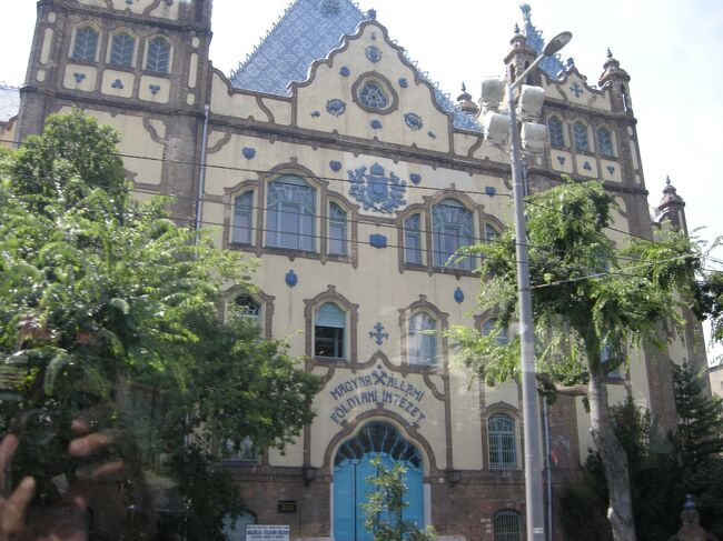 ホテルのロビーに預けていたで荷物を持ってバスに乗り、<br />みんなで旧市街観光ツアーのスタートです。<br /><br />バスはアンドラーシ大通りを抜けて英雄広場に向かった。<br />これは「地質学博物館」　窓からの撮影。<br />紺色と黄色のタイル使いがなんとも素敵で窓もユニーク！