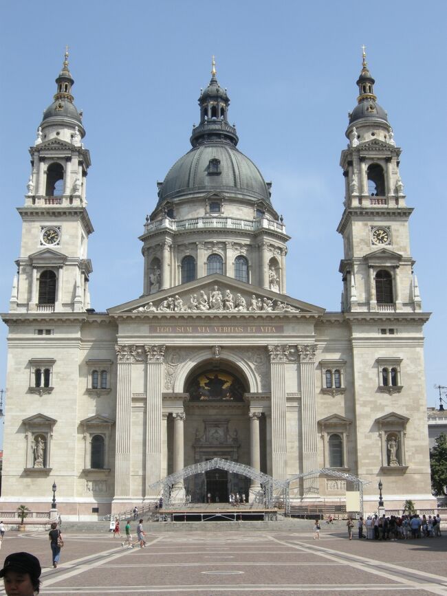 バスを降りて少し徒歩で移動し、また「聖イシュトバーン大聖堂」にやってきた。<br />ブダペストでは、国会議事堂と並んで最も高い建造物。<br />当然入るのかと思ってたが、今回は内部の見学はなかった。<br /><br />カトリック教会として19世紀半ばに着工、今世紀初頭に完成。<br />キリスト教の布教に専念した初代国王聖イシュトバーン1世に因んで<br />聖イシュトバーン大聖堂、と名付けられた。<br />新古典主義様式という建築様式で、正面に大きな鐘楼が2つあるのが特徴。