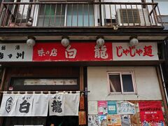 盛岡城跡公園横を通って、1953年創業盛岡じゃじゃ麺発祥の店“白龍 本店”へ。
13：00少し前に到着すると10人程度の行列が出来ていたので最後尾に並んでいたら、スタッフがオーダーを取りに来たけどMenuはじゃじゃ麺(特・大・中・小)+ちいたんたんの有無・ロースー麺(大・中・小)・焼きぎょうざ・水ぎょうざだけ。
ちなみにどの人も示し合わせたように、じゃじゃ麺+ちいたんたんの組合せで注文していた。
店内は白龍の暖簾分の幅しかなくて、カウンター席とテーブルが置かれていて通路も身体を細める必要があり本当に狭く、夏だからまだサッと座れるけど、アウターを着ている季節だと案内前に脱いで膝に抱えておかないと本当にスペースが無い。