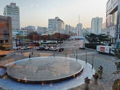 韓国到着翌日の朝、東横イン仁川富平の２階食事スペースから見た富平駅周辺の様子です。右手に少し見えているビルが首都圏電鉄富平駅の駅ビル、正面が富平駅のバスターミナルやタクシープールです。
左下の舞台の様なスペースはよくわからないですが、日中は人が集まったりするスペースになっているみたいです。