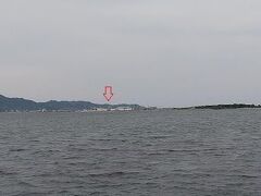 17時、中海にある大根島の寿物産の前に来た。この辺りからダイハツのテレビCMで有名になった江島大橋、通称「べた踏み坂」が良く見えるという。寿物産の前の土手に上がってみたら遠くに江島大橋が見えた。通常のカメラで写真を撮るとこのようにどこにあるのかわからないくらい小さく見える(赤矢印の下)