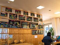 崖観音のあと近くの「道の駅とみうら」に寄り、「枇杷倶楽部」にて残った地域クーポンを使ってお土産を購入しました。お腹が空いたので道の駅で植栽の手入れをしていたスタッフの方におすすめのランチのお店をお訪ねし、魚が好きなら、とご提案いただいたのが、ここ「おさかな倶楽部」です。

道の駅から近くの富浦新港にあって、午後２時少し前に着き営業時間に間に合いました。昼のみ午後３時までの営業のようでした。
後日調べましたら列になって待つことも多いかなりの人気店のようで、この日は空いていてすぐ注文できラッキーでした。

富浦漁協直営の “浜の台所・おさかな倶楽部”。
水揚げされたばかりの魚介を使った定食料理のお品書きボードが壁に並びます。メニューはその日の獲れ具合によるんでしょうね。１食または２食限定となっている料理も多くてこの時間、ご覧のように半分以上が“完売”となっていました。