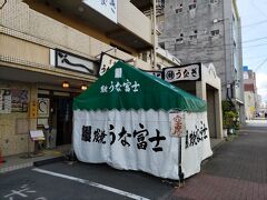 バスが東郊通1丁目バス停に着いたのは、12時を過ぎていた。ここから通常なら徒歩5分程度だが、妻の脚では倍ほど掛かってしまう。何とか急がせたが、妻の息が切れるばかりで中々進めない。ついには東郊通2丁目の大きな交差点で信号が変わるのに焦って横断歩道上で転んでしまい、多くの車を待たせる羽目になってしまった。このままでは予約がキャンセルとなる12時10分に間に合わないので、途中で妻に後からゆっくり来いと言い残して、うな富士の店舗に急いだ。丁度12時10分に到着し、何とか間に合った。席への案内を待っているうちに妻も到着した。
写真はうな富士店舗前に作られた待合室、5人ほどの人が待っていた。