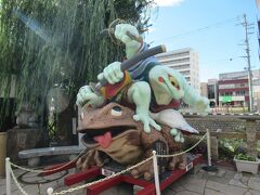 千歳橋手前の大名町通り沿いに色鮮やかな大きな蛙のオブジェがあります。ガマ侍です。茶色いガマガエルの上に着物を着て隈取した緑の蛙二匹が乗っている躍動感あふれるオブジェです。2005年東京藝術大学学生が寄贈し、2021年に修復したと記されていました。オブジェの横に蛙の石像と柳の木があります。柳の枝葉がガマ侍の背景になり、芝居のようでした。
