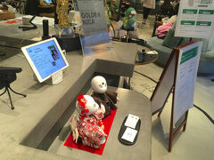 入店すると、受付前に身長20cmほどの卓上タイプのロボットが2台。
受付カウンターの中にはもう少し大きい、身長120cmほどのサイズのロボットが1台。
そのロボットが「いらっしゃいませ」と語りかけてきました。
