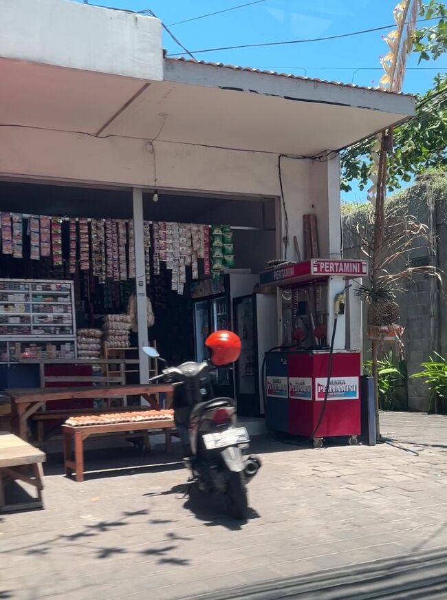 沿道にある雑貨屋の多くに、謎の黒っぽい液体を売っているらしいスタンドが置いてあります。気になったのでドライバーさんに聞いてみたところ、バイクにガソリンを給油するスタンドとのことです。<br />ガソリンスタンドよりも割高ですが、ガソリンスタンドはいつも混んでいて並ぶので商売になるそうです。<br />インドネシアも産油国のためか、ガソリン代は日本よりは安いです。<br />ドライバーさんはそれでも我々には高いと不満気でした。カーチャーターのドライバーは手取りの中からガソリン代を払うそうです。