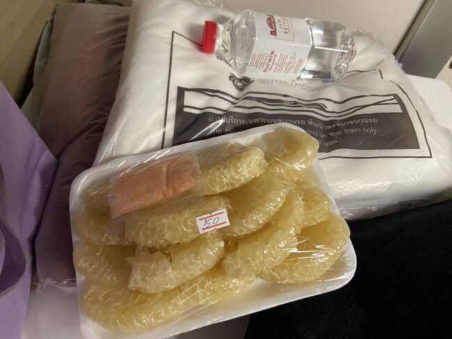 オートーコー市場で夕方、<br />安くなっていたザボンを買っていてよかったよ<br /><br />夜中にお腹空いたらこれをかじろう<br /><br />水は一人一本ついてます<br />小さめでちょうどいいサイズです<br /><br />水の下にあるのはブランケットとバスタオルです<br /><br />シャワー室はないですが・・。<br /><br />座っていると<br />「明日の朝はコーヒーとオレンジジュース　どちらがいい？両方？」<br />と聞いて回る駅員さんが度々（しつこいくらい何度も）いらっしゃいました<br /><br />正解は「どちらも要りません」です<br />どちらかを選んではいけません<br /><br />ばばあが食堂車に行っている間に<br />下段の欧米女性がばばあの分の<br />コーヒーとオレンジジュースを頼んでおいてくださったようで<br />チェンマイ到着前にひと悶着ありました<br /><br />駅員さんの言い方だと無料だと思ってしまいますもん<br />下段の方は優しいだけで悪くないですよ