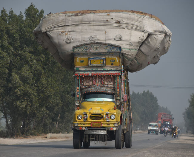 (24)籾殻を積んだ「デコトラ」(1/14「第4日目」13:30)<br />〇この写真を撮影する前(1/14午前中)大々的に『デコトラ』に『もみ殻を積込む現場』を見ており、そこで積み込まれた「籾殻」を運んでいるのだろう・・・。<br />〇「籾殻」はパキスタン各地の「レンガ工場」で「レンガ」を燃やすために使用するもの。<br />〇百舌鳥八幡宮(堺市)の「布団太鼓」が走っているようだ。(※日本では道路交通法第57条(乗車又は積載の制限等)違反間違いなし（笑）)<br />〇我車は給油のため「ガソリンスタンド」で停車中。<br />〇道路はモヘンジョダロからハイデラバードに向かうハイウェイである。<br />