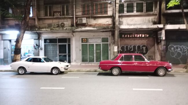 あれー<br />セブンイレブンの並びに昔の良く見た車が並んでるじゃないですか。<br />赤いのはコンパクトベンツ。<br />Eクラスベンツの前身になった車ですね。<br />途上国などでは今でも現役で活躍していますが流石にタイでは珍しくなった。<br />