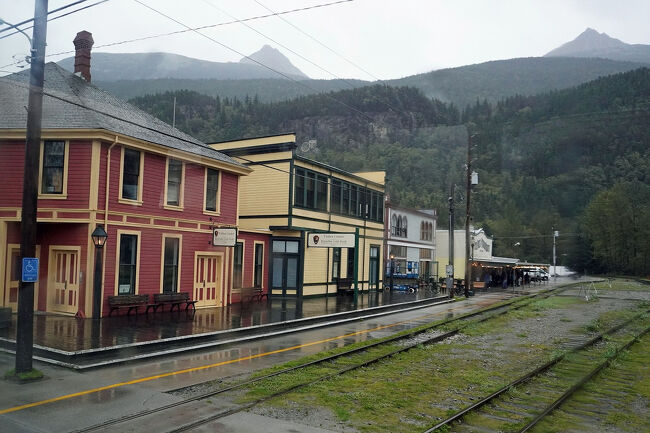 ゴールドラッシュ時代を思わせる建物の並んだ奥に鉄道駅のプラットフォームが見え、たくさんの人の姿も見えます。