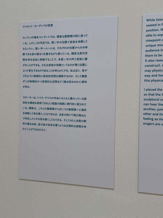 解説パネル<br />書き起こしておきます<br /><br />「ジャネット・カーディフの言葉<br />たいていの場合コンサートでは、観客は聖歌隊の前に座っている。しかしこの作品では、歌い手の位置で音楽を体験してもらいたい。歌い手一人一人は、それぞれの位置からのみ体験できる音の重なりを聴きながら歌っている。観客は展示空間全体を自由に移動することで、各歌い手の声と密接に繋がることができる。それは音楽の体験というものが聴く位置によって変化するものであることを明らかにする。私はまた、音がどのように物理的に彫刻的空間を構築するのか、そして観客がこの物理的かつ仮想的な空間をどう動き回るのかに興味がある。<br />スピーカーは、トマス・タリスの作品にもともと備わっている彫刻的な構造を実感できるよう部屋の周囲に楕円形に配されている。観客は、こちらの聖歌隊から向こうの聖歌隊へと場所を移動して音を聴くこともできれば、自身の周りで飛び跳ねたり呼応したりする音を聴くこともできる。そして40人全員の歌声が重なる時、音の波が身体を覆うような圧倒的な感覚を味わうことができるだろう。」