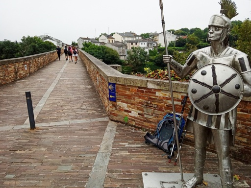 前に泊まった時は城壁の中のアルベルゲだったので、町の中に点々とある矢印を追っているだけでルーゴの外に出られるローマ橋に出られたが、今日の私営は城壁の外側なのでローマ橋に行く道筋が分かりません。わざわざ公営アルベルゲまで戻るのも癪なので勘で歩いていると大分遠回りになったようだがローマ橋に辿りつけました。<br /><br />ローマ兵士が私のバックパックの番をしています（嘘）。<br />このローマ兵士の像、どう見てもスケルトン兵士にしか見えませんよ。こんなのが突然動いたら怖いですねー。兵士の像も嘘っぽいけど橋自体もこれ本当にローマ時代の物なの？それにしては洗練されすぎるんですけどね。現代の技術で同じ位置に再現しただけじゃないの？（勝手な想像です）