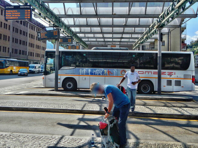 ドモドッソラ駅前のバスターミナル。ここでマクニャーガ行きのバスを約1時間待つ。<br />プラットフォームがいくつもあるが、ここに来るほとんどのバスはCOMAZZI社のものだ。(マクニャーガ行きのバスを待っている間に、ブリークからシンプロン峠を越えてきたスイスのポストバスが到着した。お客を下ろした後、写真左端に止まっている。)<br />マクニャーガ行きのバスは12時10分発。3番のプラットフォームから出発する。前に停まっているバスがそれでスーツケースはバスの横腹に入れられる。