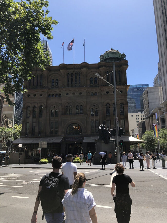 そのマイヤーの前にシドニーが最も美しかった時代に建設された美しいショッピングアーケードビルQVB(クィーン ビクトリア ビルディング)が見えます。<br /><br />入口に名前の道りビクトリア女王の銅像が建っています。<br /><br />1898年創業のこのビルは当時イギリスの国王だったビクトリア女王の即位50周年を記念して建てられました。<br /><br />この入口のビクトリア女王の座像は待ち合わせのメッカです。<br />