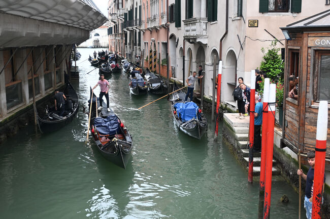 午前中は小雨がぱらついており、少し遅めの出発。長袖が必要なほど気温も低く、ゴンドラもまだあまり稼働していない。ゴンドラの操縦士はゴンドリエーレといい、なるためには操縦技術のほかに語学や歴史を学び、業界団体の資格的なものを取得する必要がある。ただ、425人という定員制があり、たとえ資格を取得しても誰かが引退しないと枠が空かないため、実際にゴンドリエーレになるのは相当の競争率とのこと。<br />