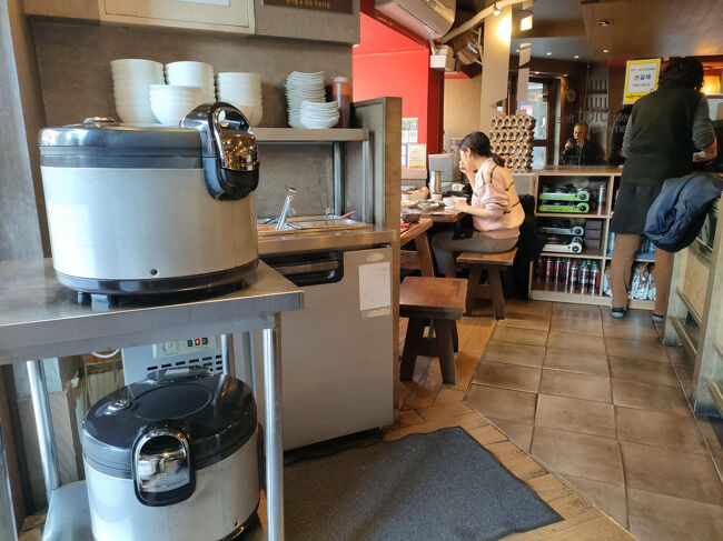 外には並んでなかったものの、中では一組（女性二人）が待ってました。僕も続いて待ちます。目の前はセルフバー、ご飯のお替りもできる巨大な炊飯器もあります。