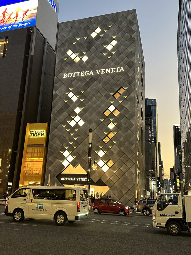 銀座って・・・こんな街・BOTTEGA VENETA 銀座フラッグシップ店<br />2018年12月8日にオープンした、アジア最大級の広さを誇るボッテガ・ヴェネタの旗艦店です。内部は、日本の伝統的な要素を取り入れたデザインが特徴です。 晴海通りから入ると、外と内をつなぐ「土間」をイメージした空間があり、鉄平石のフロアからオーク材のフローリングへと変化します。 また、「折り紙」をイメージした窓や壁面の幾何学的な形状、左官職人が漆喰を塗った壁面など、日本の職人技が随所に光る洗練された空間となっています。 来店客を非日常へと誘い、心を込めてもてなすという日本的な精神が建築全体に表現されています。