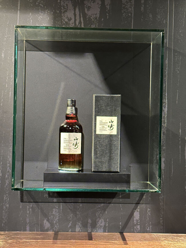 日比谷BAR WHISKY-S・バーカウンター背面<br />山崎25年とそのカートン（箱）が飾っています。「山崎25年」の定価(700ml)は360,000円(税別)です。 税込価格では396,000円になりますが、「山崎25年 ミズナラ」は約1,600,000円で取引されているとされています。