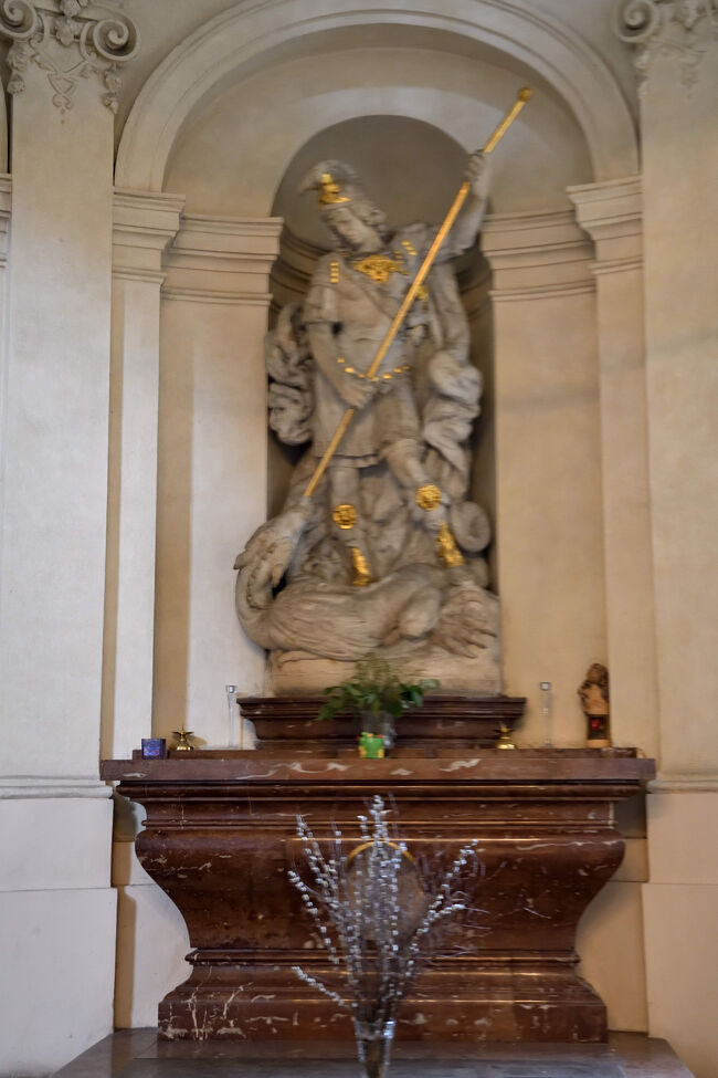 聖ミクラーシュ教会の一角<br /><br />ミカエル像の足元には枝と黄色いリボンが添えられていて、静かな祈りの場になっていました。